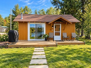 A wooden cabin with a deck, a sliding glass door, and two chairs.