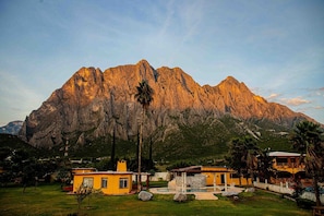 Un paysage montagneux avec un bâtiment jaune doté d’une piscine et d’un ciel dégagé.