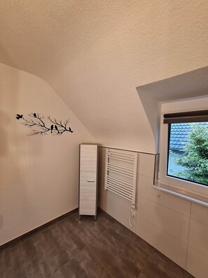 Habitació amb un radiador, una finestra que dona a vegetació i una decoració mural amb ocells a la branca.