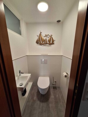 Un baño pequeño con inodoro, lavamanos y una decoración náutica: un cuadro de un velero.