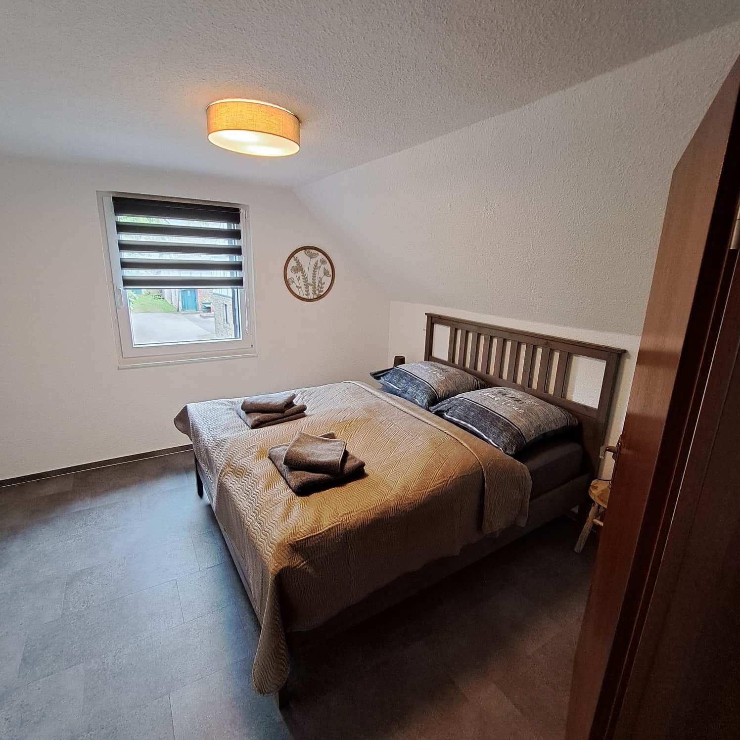 Un dormitorio con cama, una ventana con persianas, un reloj de pared y una lámpara en el techo.