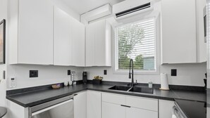 Una cocina moderna con armarios blancos, encimera negra, lavavajillas de acero inoxidable y ventana con persianas.