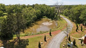 Un paisaje rural con un camino sinuoso, un estanque y varios árboles.