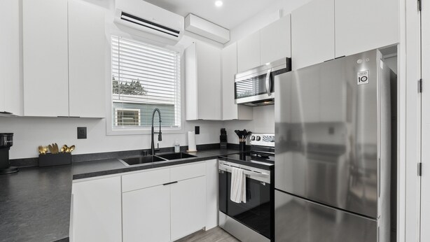 Una cocina moderna con armarios blancos, un refrigerador de acero inoxidable, horno integrado y una ventana con persianas.
