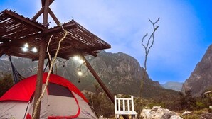 A tent with a wooden structure overhead, a white chair, and a rocky landscape with mountains in the background.