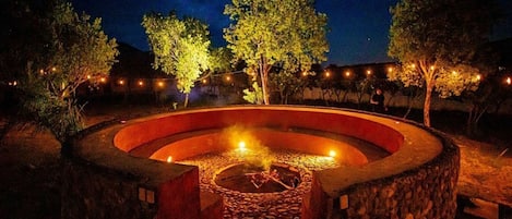 A circular stone fire pit with a central fire, surrounded by a low stone wall.