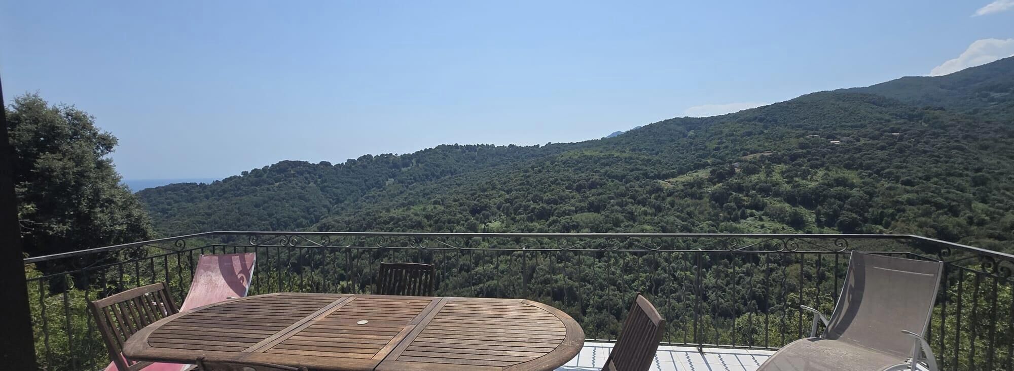 Un balcón con mesa y sillas con vista a una montaña boscosa.