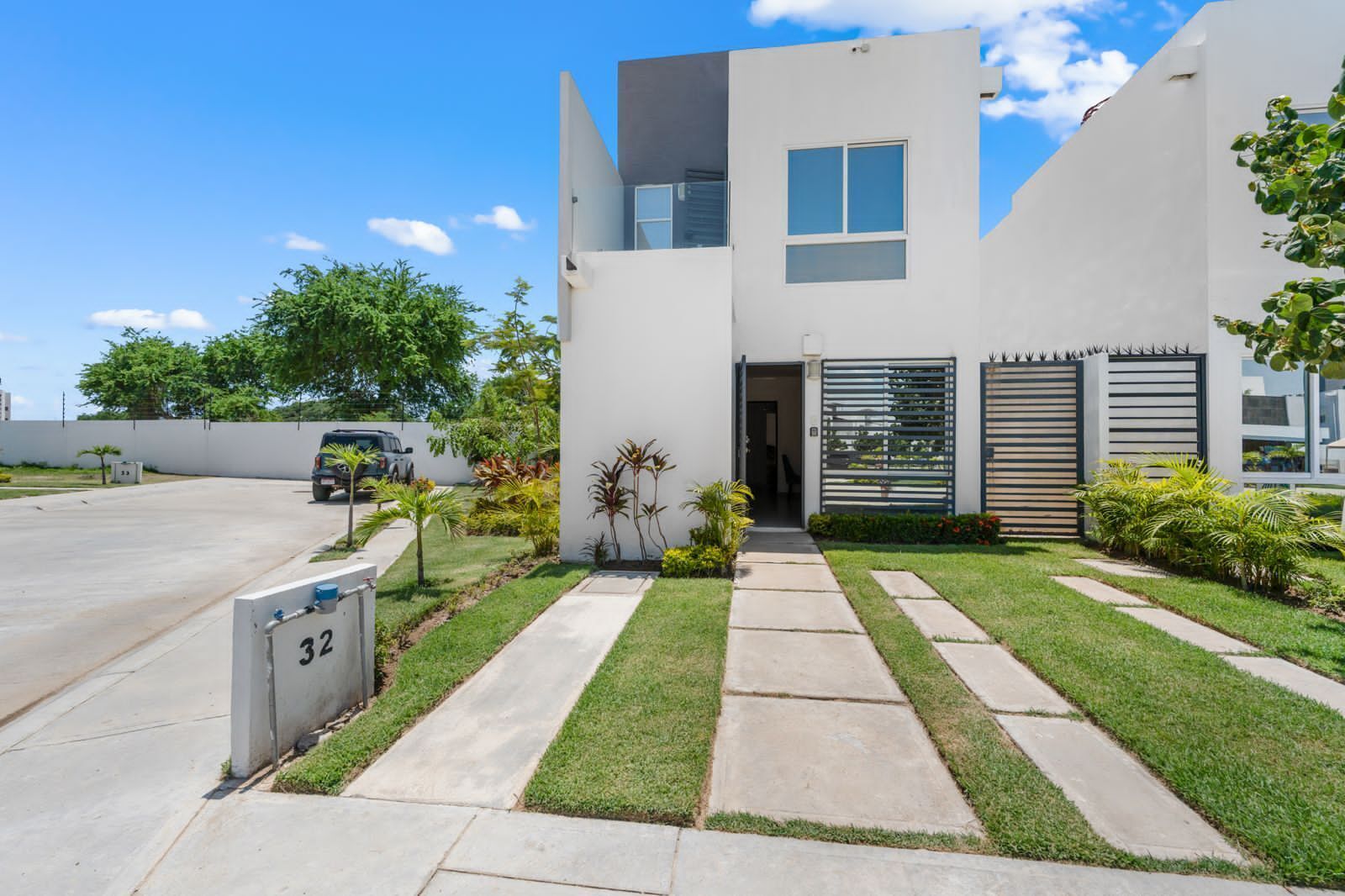 A modern two-story house with a paved driveway, a gated entrance, and a well-maintained lawn.