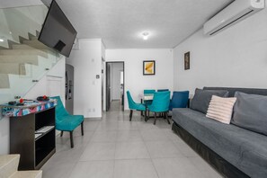 A modern living room with a grey sofa, teal chairs, a flat-screen TV mounted on the wall, and a staircase leading to another level.