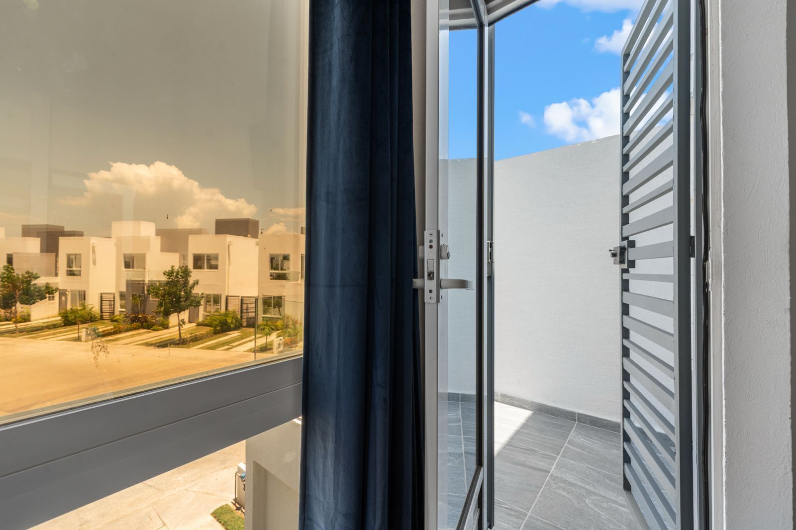 A view from a balcony with a glass door leading to a modern building with white walls and a tiled floor.