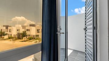 A view from a balcony with a glass door leading to a modern building with white walls and a tiled floor.