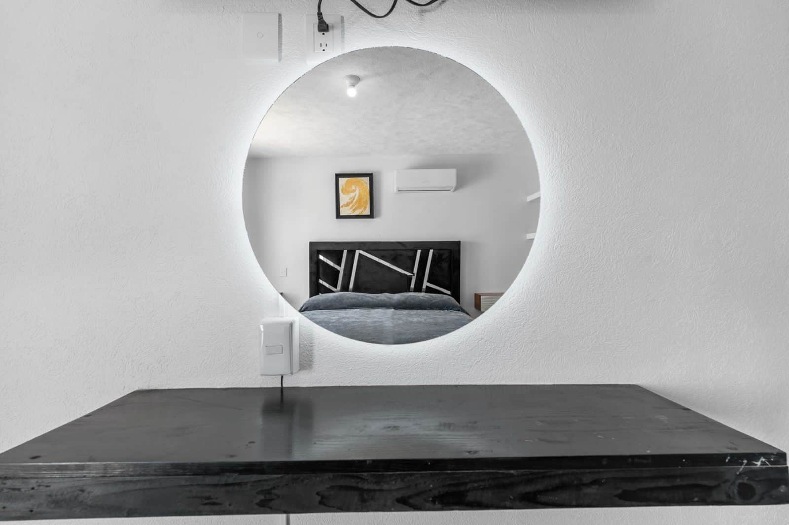 A circular mirror on a wall with a bed and a framed picture in the reflection.