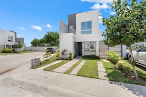 A modern two-story residential building with a driveway, a gated entrance, and a well-maintained lawn.
