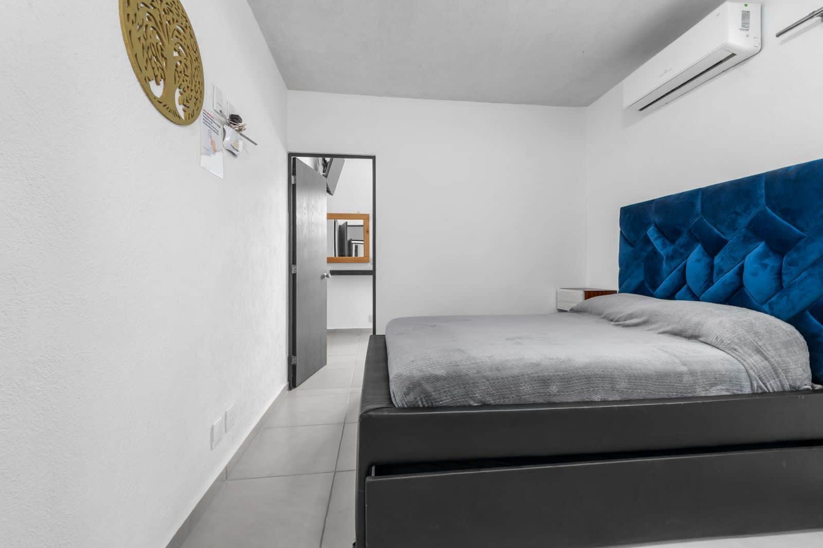 Un dormitorio con cama, aire acondicionado, decoración en la pared y puerta que da a otra habitación.