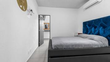 Un dormitorio con cama, aire acondicionado, decoración en la pared y puerta que da a otra habitación.