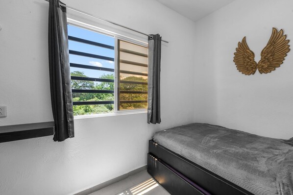 A bedroom with a bed, a window with curtains, and a wall-mounted decorative item.
