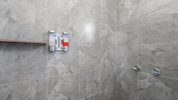 Zona de ducha con azulejos de mármol gris, un cabezal de ducha y dos dispensadores fijos en la pared etiquetados 'champú' y 'gel de baño'.