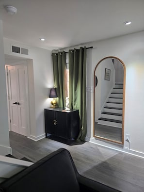 A hallway with a black console, green curtains, a white door, and a staircase with a mirror. - Serene 2-bedroom townhome with AC in vibrant Dallas (Dallas)
