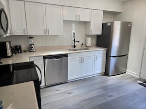 A modern kitchen with white cabinets, a stainless steel refrigerator, a dishwasher, and a coffee maker. - Serene 2-bedroom townhome with AC in vibrant Dallas (Dallas)