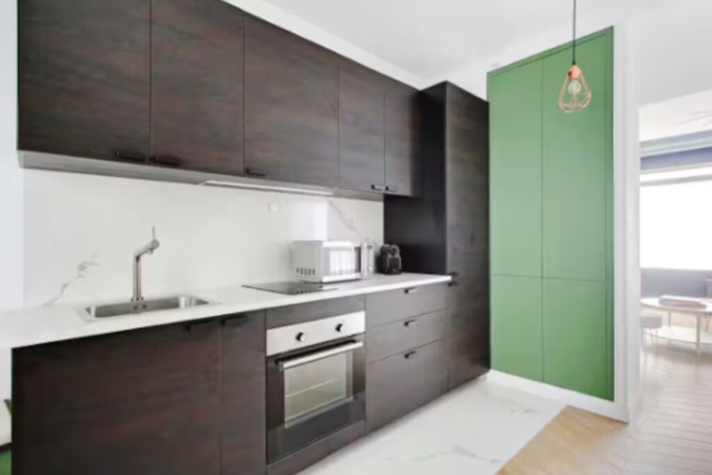 Una cocina moderna con armarios oscuros, una encimera blanca y un horno empotrado.