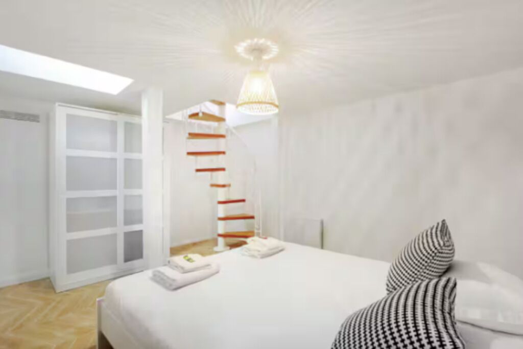 A bedroom with a bed, a white door, a staircase, and a hanging light fixture.