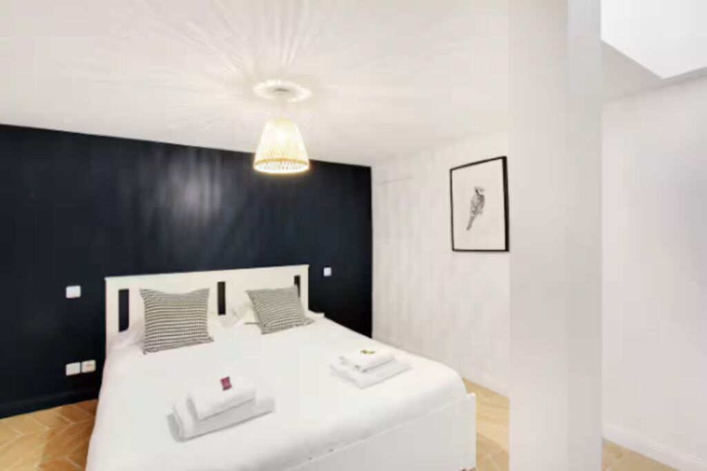 Een moderne hotelkamer met een groot bed, een plafondlamp en een ingelijst schilderij aan de muur.