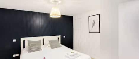 Quarto de hotel moderno com uma cama grande, luminária no teto e um quadro na parede.