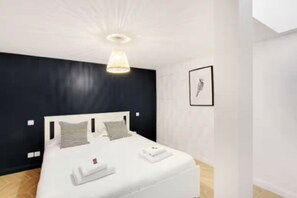 A modern hotel room with a large bed, a ceiling light fixture, and a framed picture on the wall. - Cozy apartment near Bastille – 1 BR / Sleeps 4 (Paris)