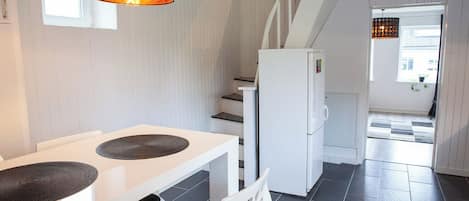 A kitchen with a white refrigerator, a dining table with two placemats, and a staircase leading to another room.