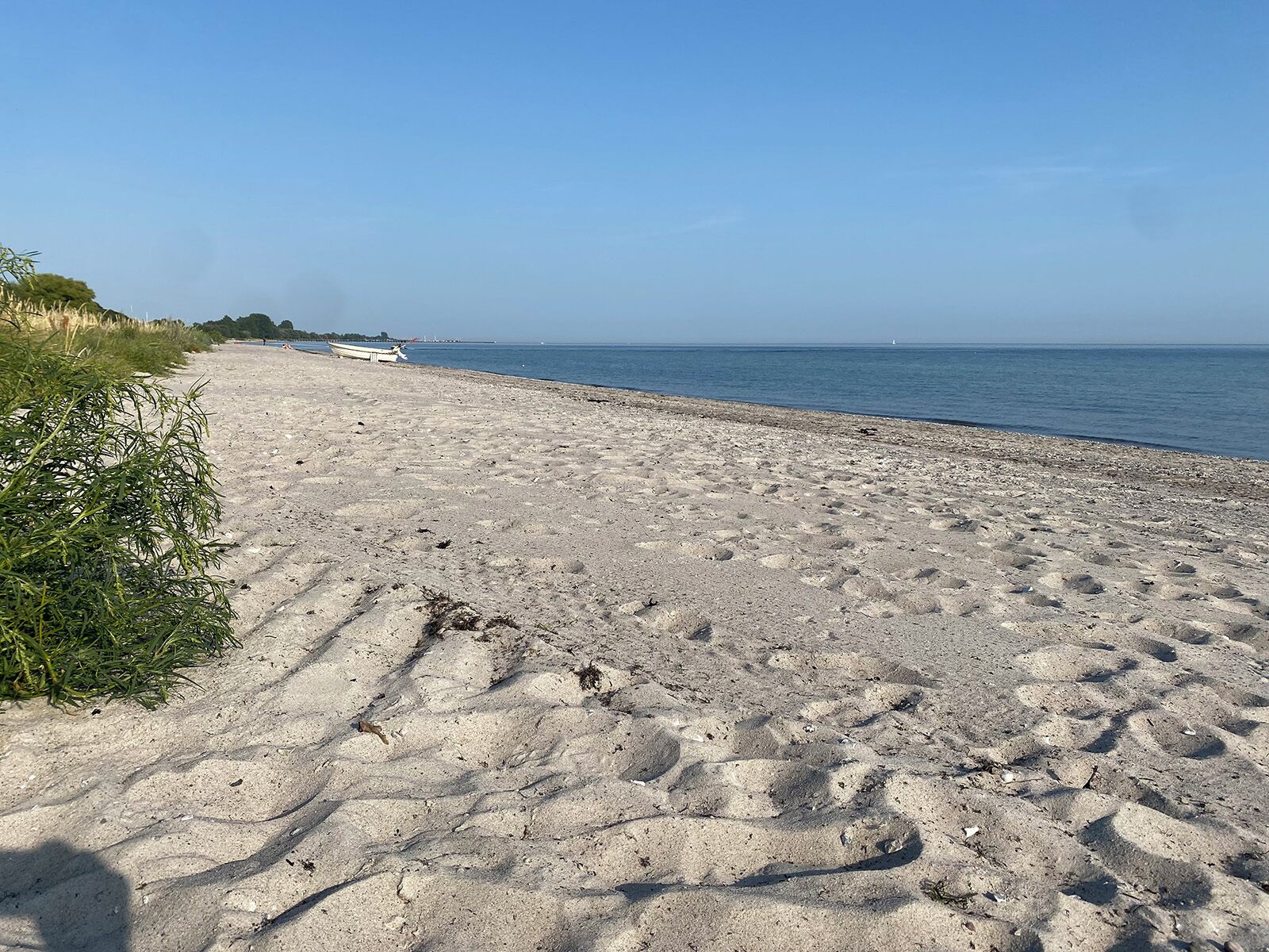 En sandstrand med en båt till vänster och stilla vatten i bakgrunden.