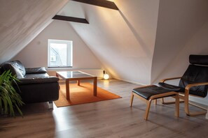 Ett modernt loftrum med en sluttande takhöjd, en svart lädersoffa, ett träbord och en svart läderfåtölj.