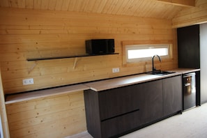 A compact kitchen with wooden walls, a black countertop, a built-in microwave, and a window above the sink.