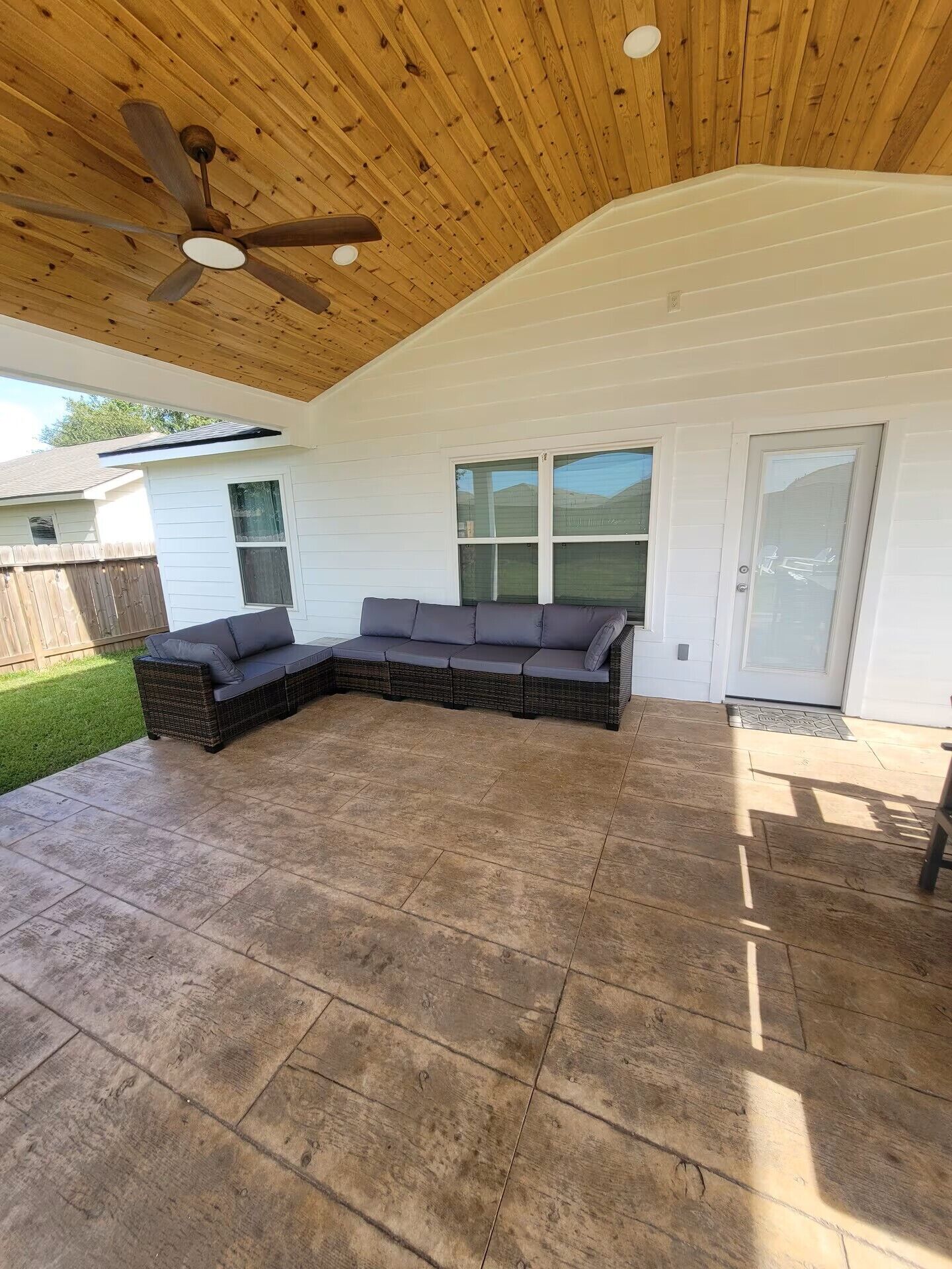 A covered patio area with a sectional sofa, a ceiling fan, and large windows.