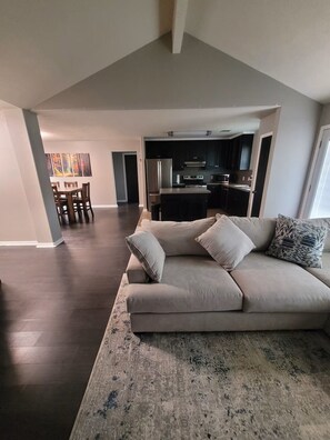 A modern living room with a sectional sofa, a dining area with wooden chairs, and a kitchen with dark cabinetry. - Fantastic 3-bedroom house with a stunning patio in charming Conroe (Conroe)