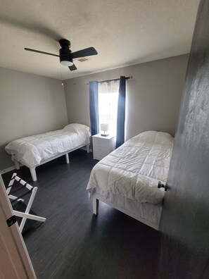 A bedroom with two single beds, a ceiling fan, a bedside table with a lamp, and a window with curtains. - Fantastic 3-bedroom house with a stunning patio in charming Conroe (Conroe)