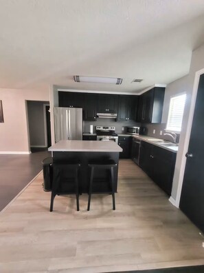 A modern kitchen with a central island, dark cabinetry, and stainless steel appliances. - Fantastic 3-bedroom house with a stunning patio in charming Conroe (Conroe)