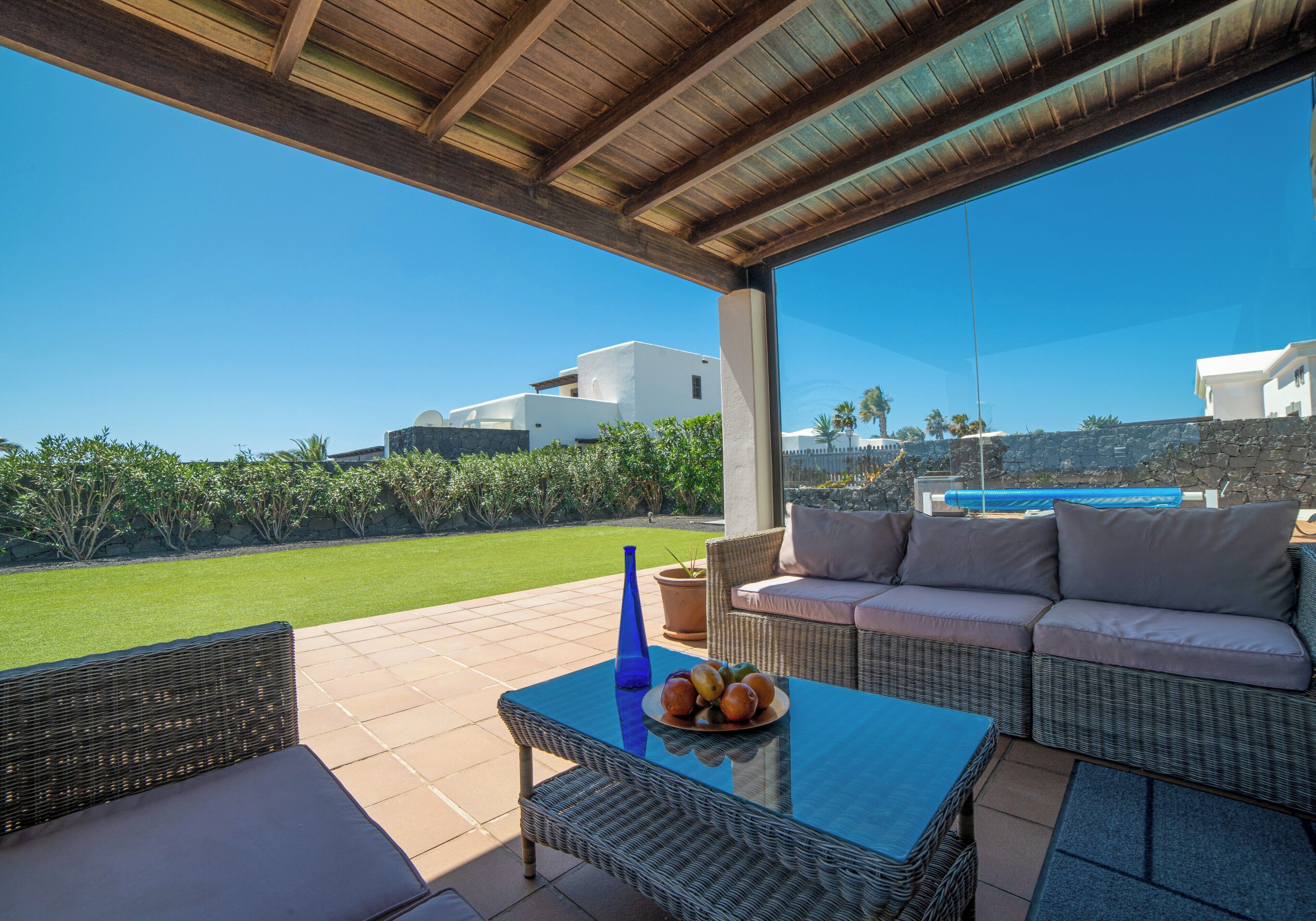 Un espace extérieur aménagé, abrité et doté d’une table, de coussins, et offrant une vue sur une piscine et sur la verdure.