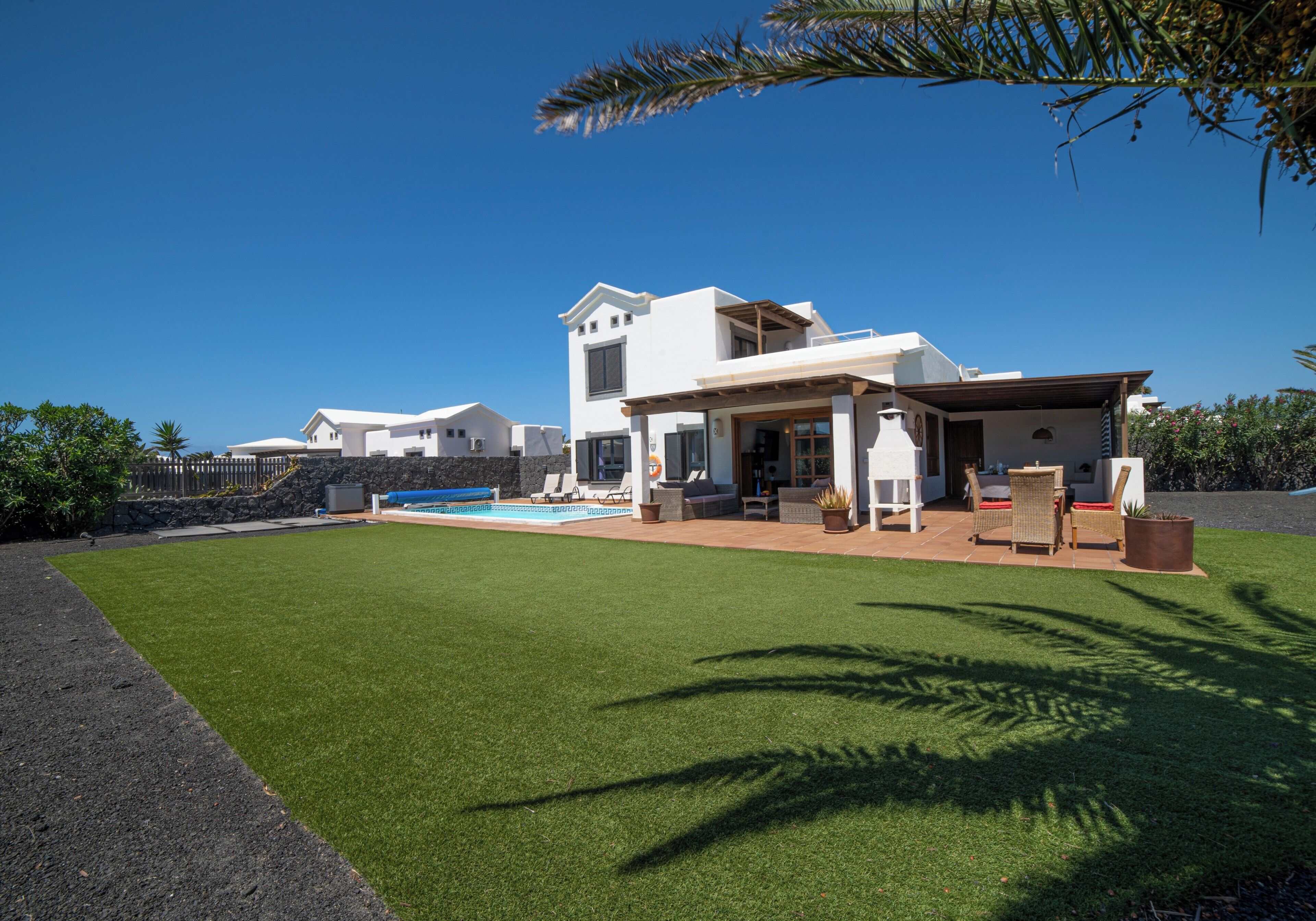 Et moderne hus med to etager, en overdækket terrasse, en swimmingpool og en velplejet græsplæne.