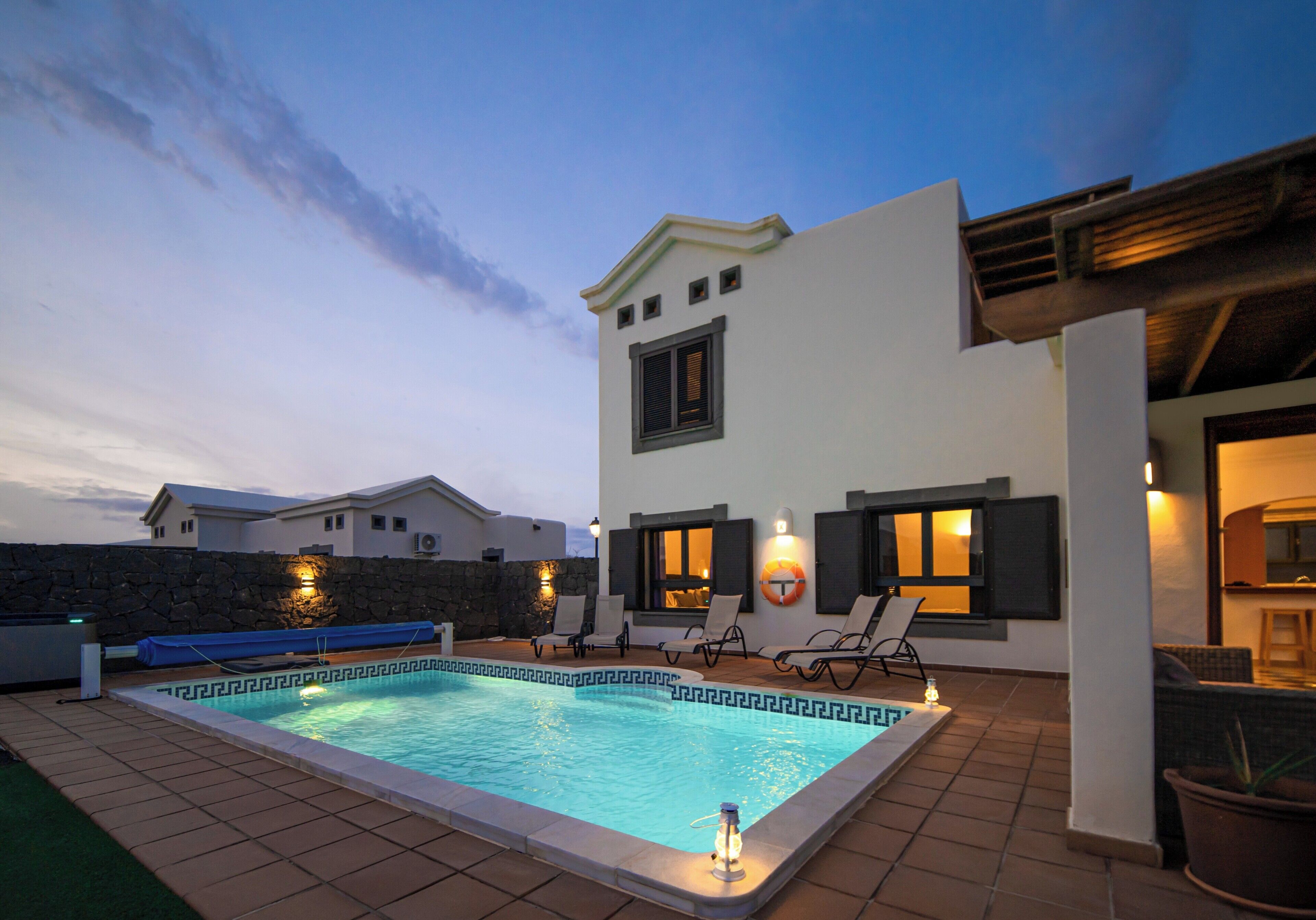 A modern outdoor pool area with a clear blue pool, surrounded by lounge chairs and a stone wall.