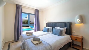 Ein Hotelzimmer mit zwei Betten, einem Nachttisch, einer Lampe und Blick auf einen Pool.