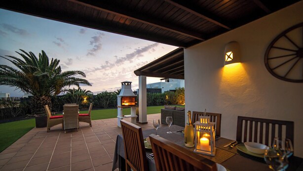 Eine Terrasse im Freien mit einem Esstisch, einem Grill und Blick zum Himmel.