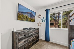 A room with a large flat-screen TV mounted on the wall, a wooden dresser with drawers, and a window with blue curtains. - 2 Suite to be good! Escape to the Mountains! (Flagstaff)