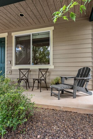 Ein überdachter Patio-Bereich mit zwei Adirondack-Stühlen, einem kleinen Tisch und einem Blumentopf.