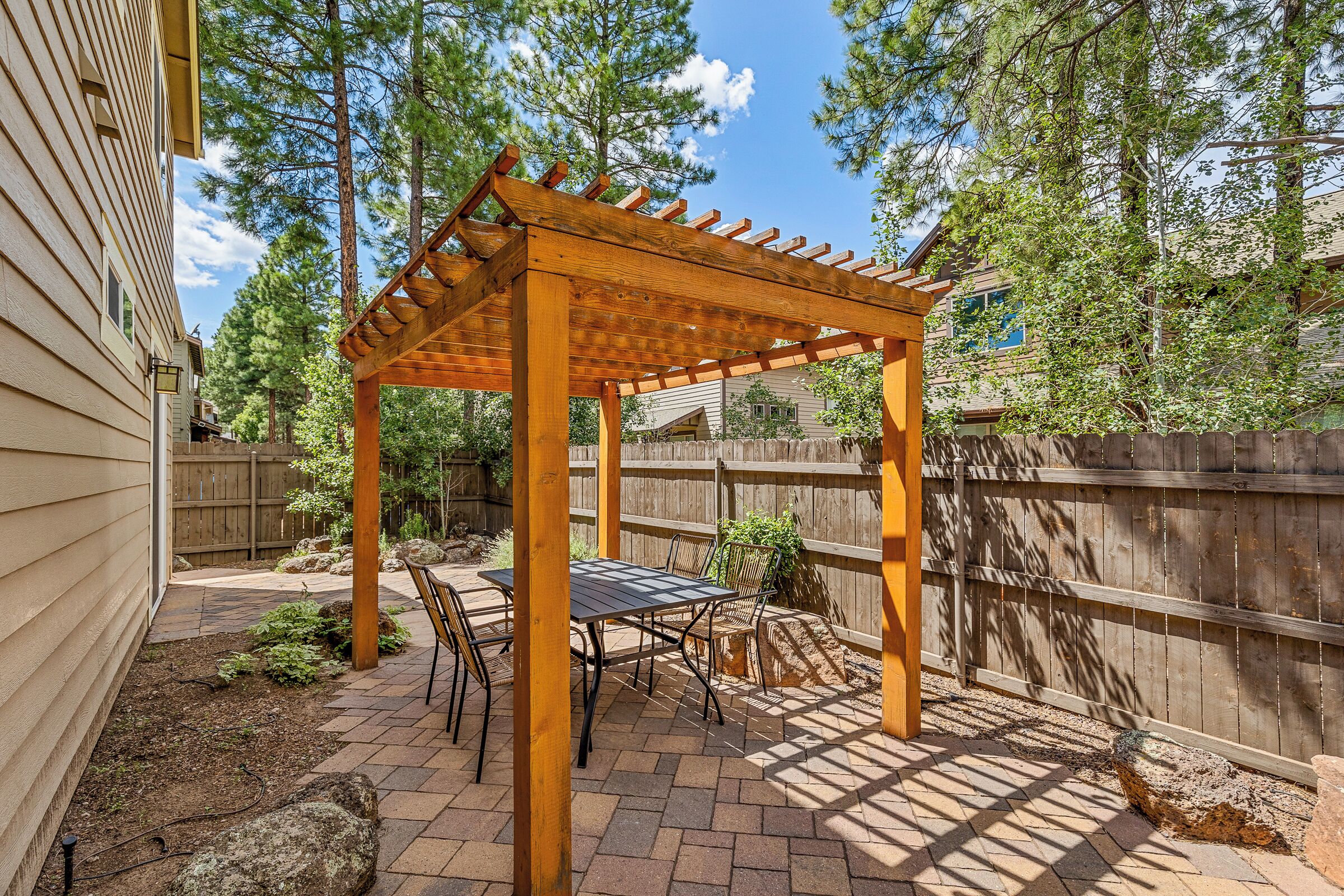 A covered patio area with a pergola, outdoor seating, and a wooden fence.