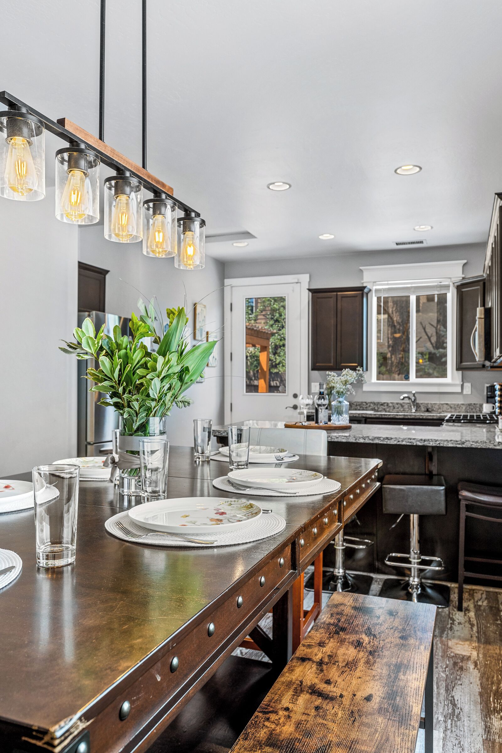 A modern kitchen with a long wooden island, pendant lighting, and a view of the backyard.