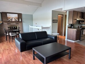 A modern living room with a black leather sofa, a coffee table, and a dining area with a brick wall and wooden railing. - Waterfront Retreat on Hammersley Inlet (Shelton)
