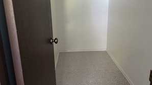 Una habitación con piso alfombrado, una puerta de madera y una pared blanca con un perchero.