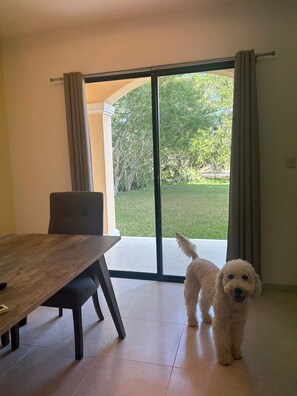A dining area with a table and chairs, a dog standing by a sliding glass door leading to a grassy outdoor area. - Yucatán Coastal Getaway | Near the Beach & Surrounded by Nature (Telchac Puerto)