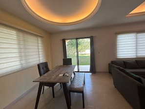 A dining area with a table and chairs, a bench, a sofa, and a sliding glass door leading to a garden.
