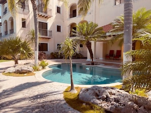 A pool surrounded by palm trees and a building with balconies.